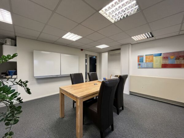 Vergaderruimte in Leidse Rijn met houten tafel, vier zwarte stoelen, whiteboard en kleurrijk kunstwerk aan de muur.